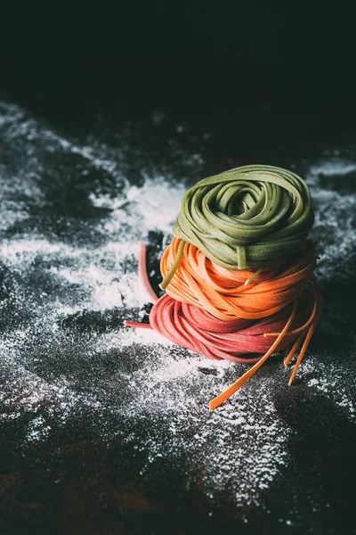 Nahaufnahme Bild von Stapel von rohen bunten Tagliatelle Pasta auf dem Tisch mit Mehl bedeckt — Stockfoto