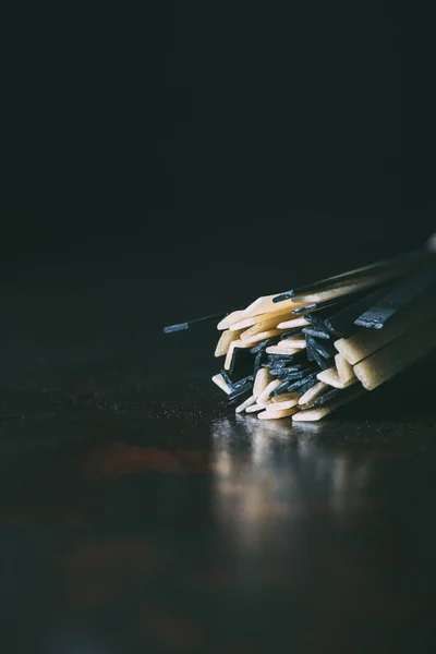 Closeup shot of raw classical and black linguine pasta on black background — Stock Photo