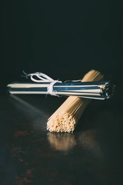 Vista ravvicinata di spaghetti crudi e linguine avvolti da nastri su fondo nero — Foto stock