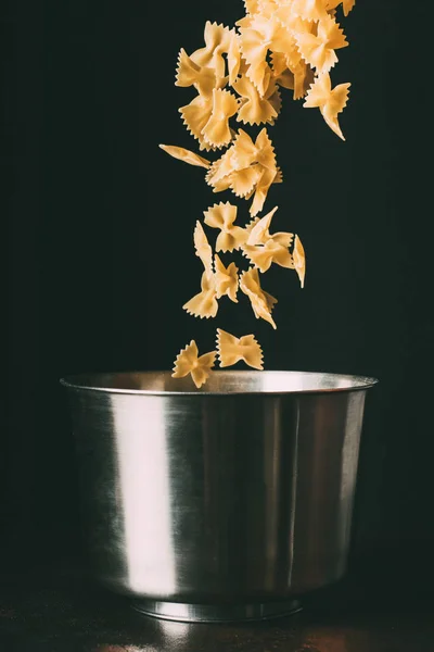 Close up view of farfalle falling into pan on black background — Stock Photo