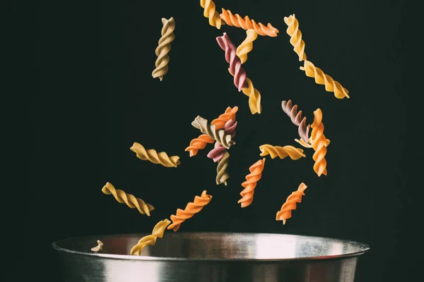 Primer plano plano de fusilli colorido cayendo en la sartén sobre fondo negro - foto de stock