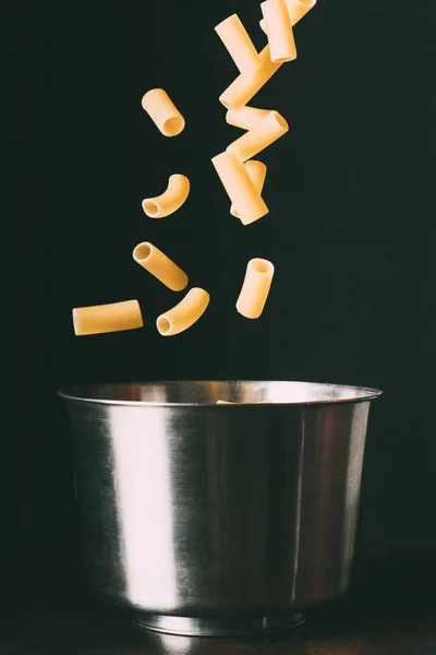 Nahaufnahme von Rigatoni, die in Pfanne auf schwarzem Hintergrund fallen — Stockfoto