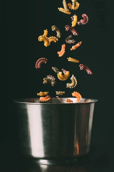 Gros plan de pâtes colorées tombant dans la casserole sur fond noir — Photo de stock