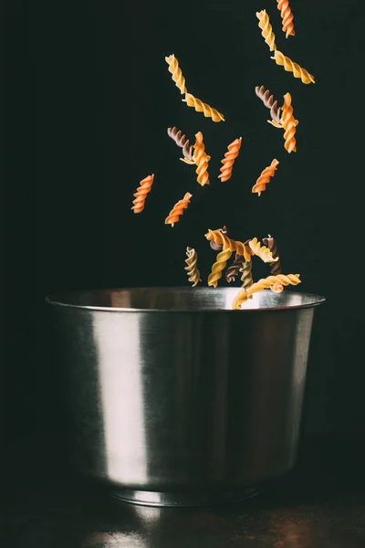 Nahaufnahme Bild von bunten Fusilli fallen in Pfanne auf schwarzem Hintergrund — Stockfoto