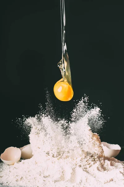 Close up view of yolk falling on flour on black background — Stock Photo