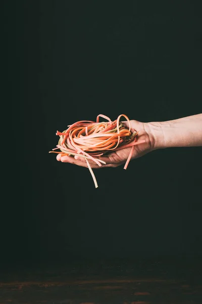 Cropped image of man holding homemade colorful raw tagliatelle on hand palm over table on black background — Stock Photo