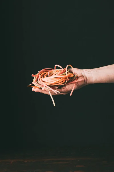 Abgeschnittenes Bild eines Mannes mit hausgemachten bunten rohen Tagliatelle auf der Hand Palme über Tisch auf schwarzem Hintergrund — Stockfoto