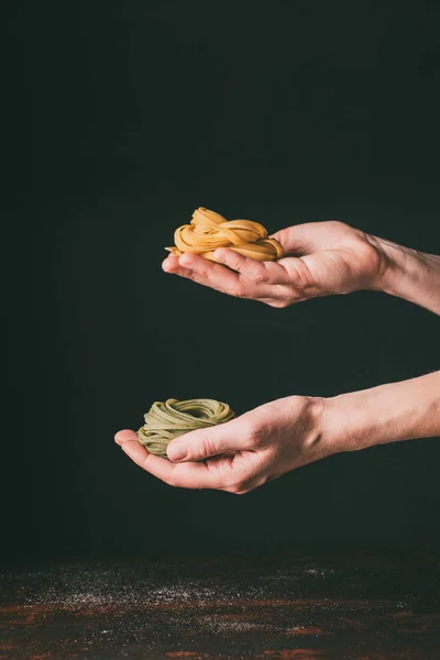 Cropped image of man holding raw tagliatelle on hand palms over table on black background — Stock Photo