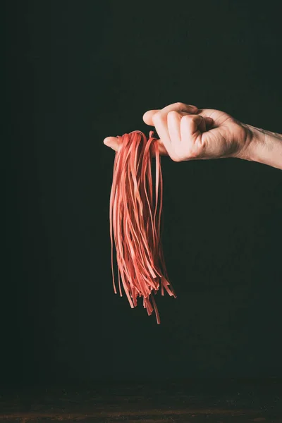 Cropped image of man holding raw red tagliatelle on finger over table on black background — Stock Photo