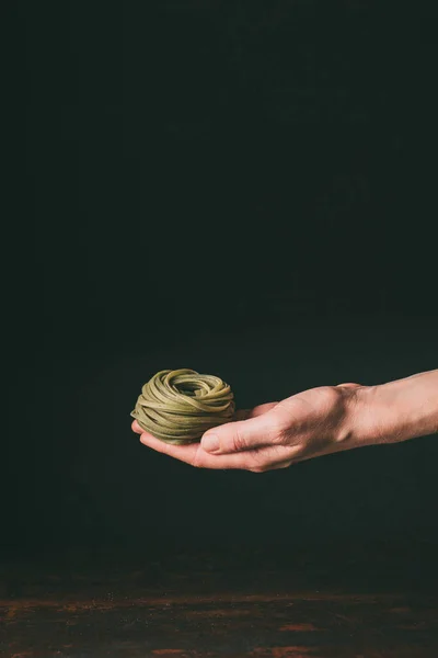 Cropped image of man holding homemade raw green tagliatelle over table on black background — Stock Photo