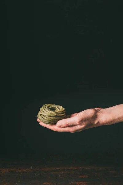 Abgeschnittenes Bild eines Mannes mit hausgemachter roher grüner Tagliatelle über dem Tisch auf schwarzem Hintergrund — Stockfoto