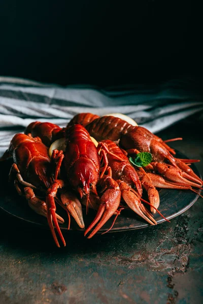 Closeup shot of pile of crayfishes with mint and lemon slices on plate and kitchen towel on table — Stock Photo