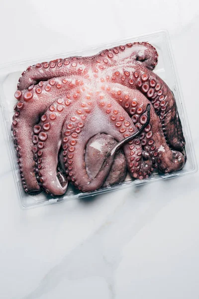 Top view of uncooked octopus in plastic container on marble surface — Stock Photo