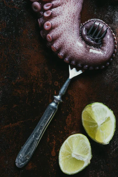 Vue de dessus du tentacule de grande pieuvre avec fourchette et chaux sur une surface métallique rouillée — Photo de stock