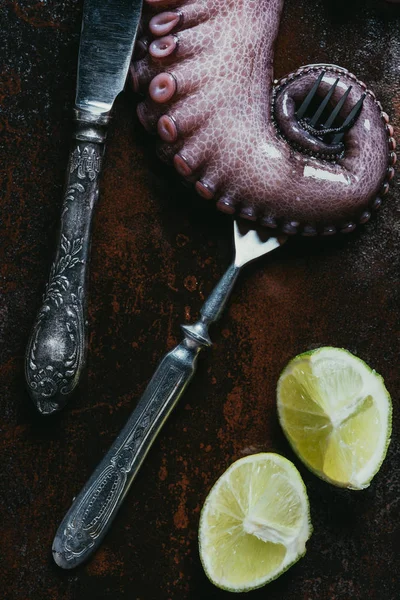Top view of big octopus tentacle with fork, knife and limes on rusty metal surface — Stock Photo