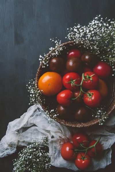 Top view of fresh red tomatoes in wicker bowl with white flowers on wooden background — Stock Photo