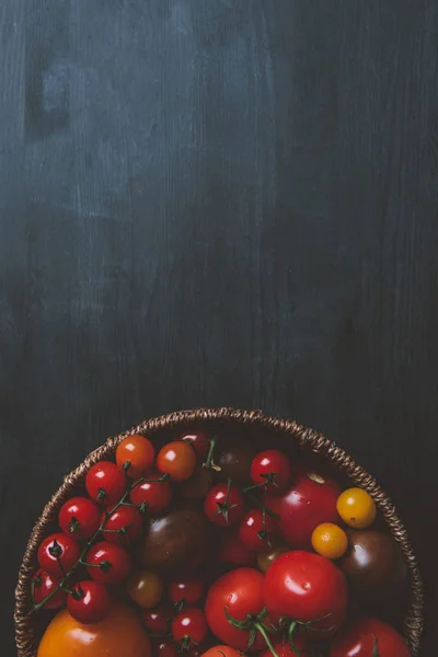 Vista superior de tomates rojos cherry en cuenco de mimbre sobre fondo de madera con espacio para copiar - foto de stock