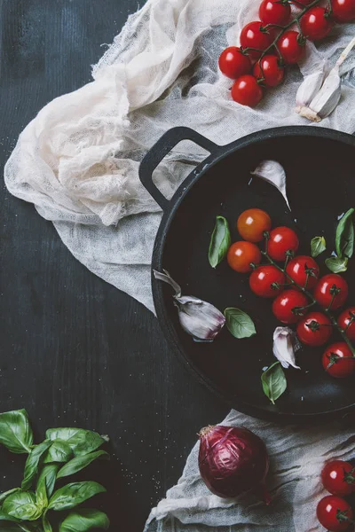 Top view of red cherry tomatoes with basil leaves in frying pan on gauze on wooden background — Stock Photo