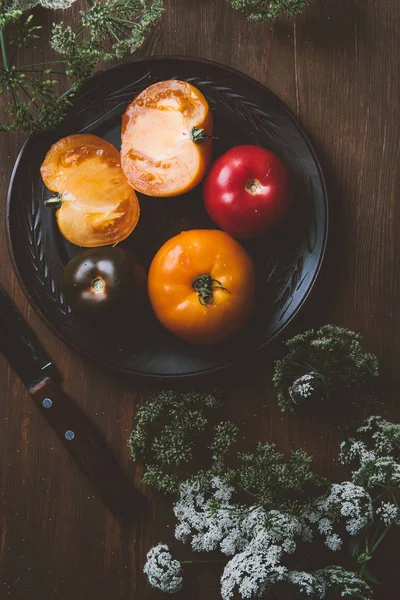 Vue du dessus des tomates sur plaque en céramique avec couteau et fleurs de persil — Photo de stock