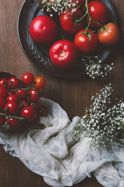 Top view of red fresh tomatoes in ceramic plate on wooden background with flowers and gauze — Stock Photo