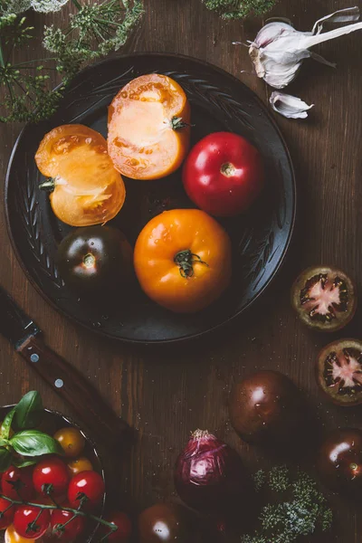 Vue de dessus de différentes tomates sur plaque en céramique avec couteau sur fond en bois — Photo de stock