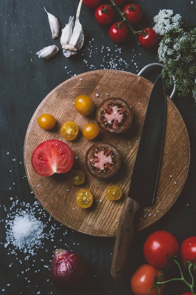 Вид зверху на чорний принц помідори і жовті вишневі помідори на обробній дошці з ножем, часником і сіллю — стокове фото