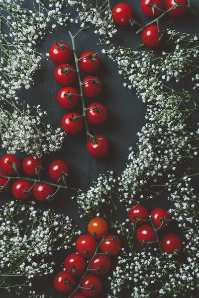 Vue de dessus des tomates cerises rouges et des fleurs blanches sur fond de bois noir — Photo de stock