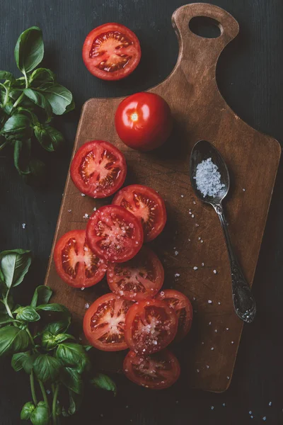 Vista superior de tomates vermelhos, folhas de manjericão e sal na colher na tábua de corte — Fotografia de Stock