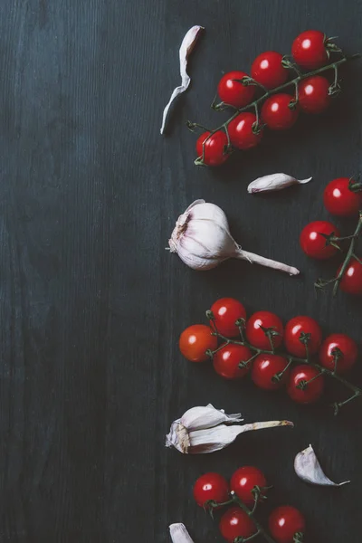 Top view of red cherry tomatoes and garlic on black wooden background — Stock Photo