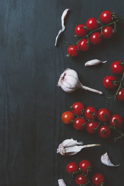 Draufsicht auf rote Kirschtomaten und Knoblauch auf schwarzem Holzhintergrund — Stockfoto