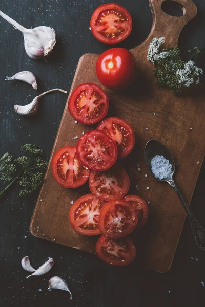 Vista superior de tomates rojos maduros, ajo, flores y sal en la tabla de cortar - foto de stock