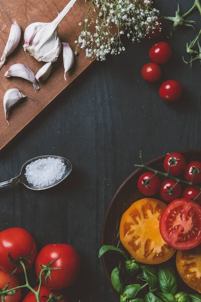 Top view of different tomatoes, garlic and salt on wooden tabletop with copy space — Stock Photo