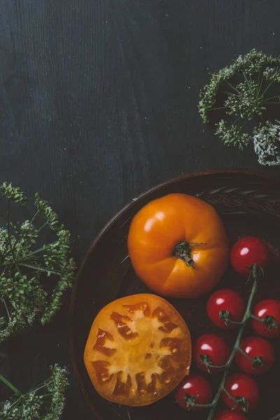 Vue de dessus des tomates cerises rouges et des tomates jaunes sur assiette avec des fleurs de persil sur fond en bois — Photo de stock