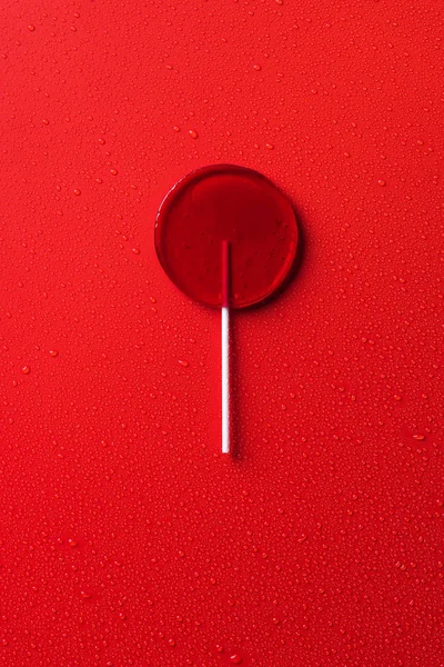 Top view of one lollipop on red surface with water drops — Stock Photo