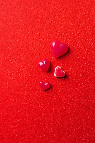 Top view of heart shaped candies on red surface with water drops — Stock Photo