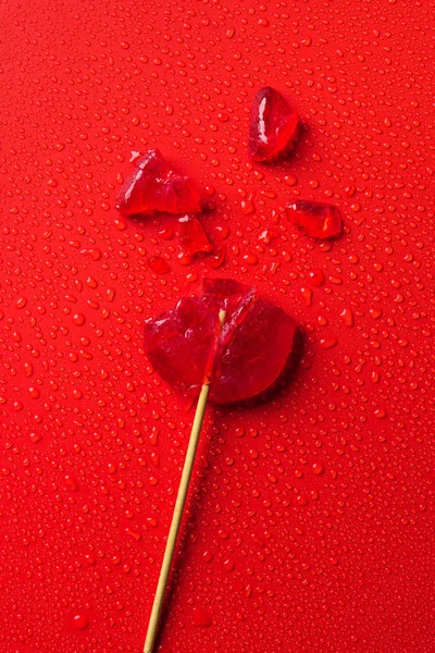 Vista superior de piruleta rota en la superficie roja con gotas de agua - foto de stock