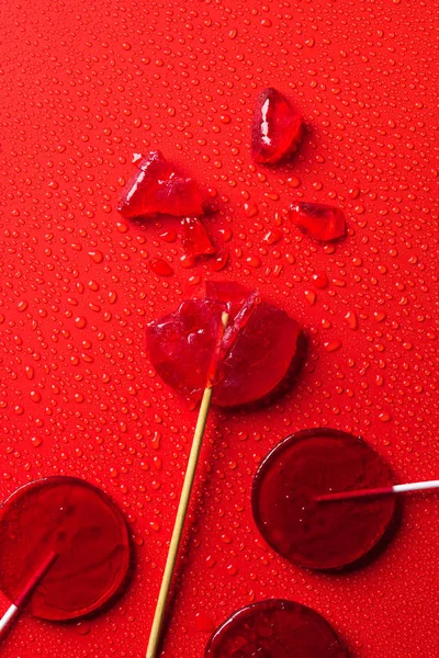 Vista superior de piruletas en la superficie roja con gotas de agua - foto de stock