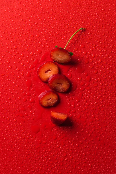 Vista superior de la fresa cortada en la superficie roja con gotas de agua - foto de stock