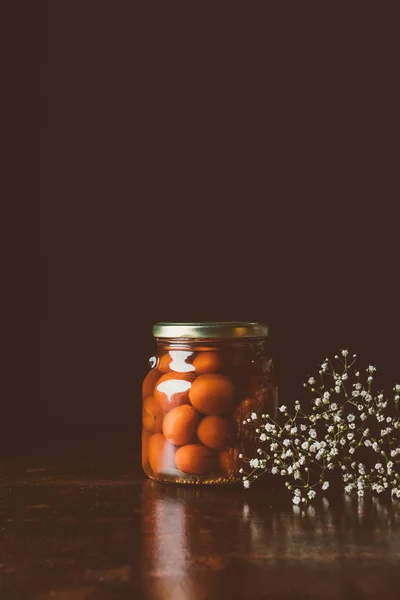 Glass jar with preserved red tomatoes on wooden table in dark kitchen — Stock Photo