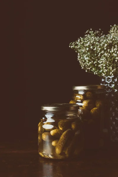 Jarros de vidro com pepinos preservados na mesa de madeira na cozinha escura — Fotografia de Stock