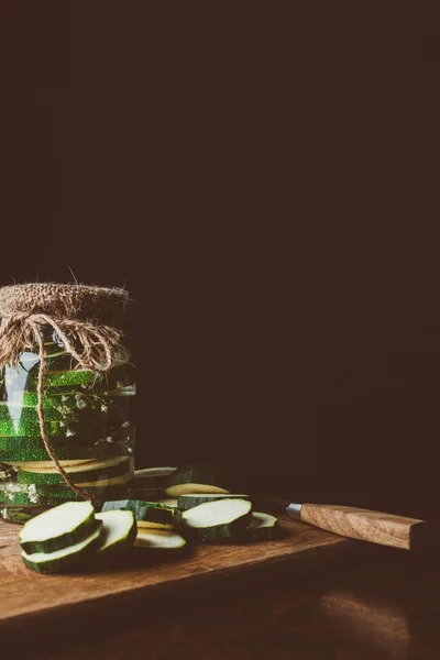 Courgettes conservées dans un bocal en verre et courgettes coupées sur panneau en bois dans la cuisine — Photo de stock