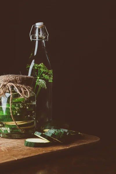 Preserved zucchini in glass jar and fresh cut zucchini on wooden board in kitchen — Stock Photo