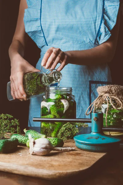 Imagem cortada de mulher preparando pepinos preservados e derramando água em frasco na cozinha — Fotografia de Stock