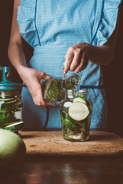 Cropped image of woman preparing preserved zucchini and pouring water into jar at kitchen — Stock Photo