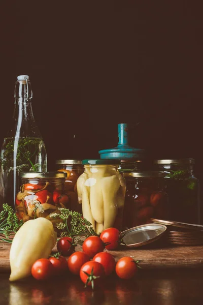 Glass jars with preserved vegetables and fresh vegetables on table — Stock Photo