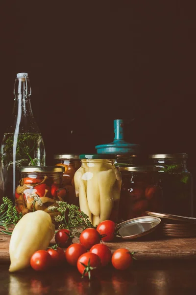 Frascos de vidrio con verduras conservadas y verduras frescas en la mesa - foto de stock