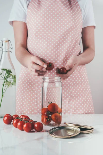 Image recadrée de la femme mettant des tomates dans un bocal en verre à la cuisine — Photo de stock