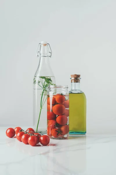 Glass jar with tomatoes, glass bottle with dill and bottle of oil on table — Stock Photo