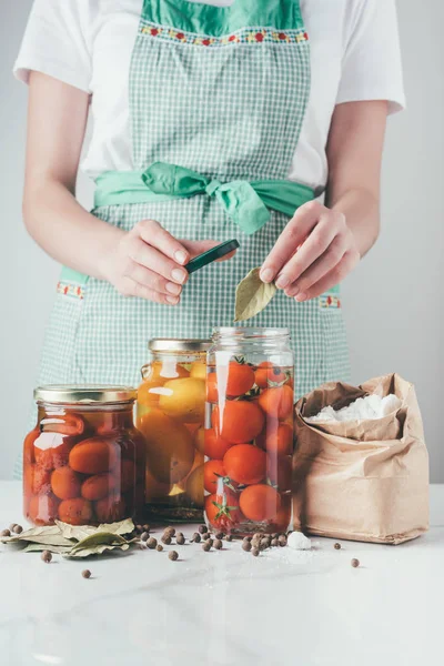Cropped image of woman adding bay leaf to preserving tomatoes at kitchen — Stock Photo