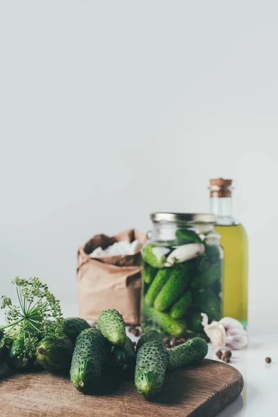 Frische Gurken auf Schneidebrett auf dem Tisch mit eingelegten Gurken im Glas auf dem Hintergrund — Stockfoto